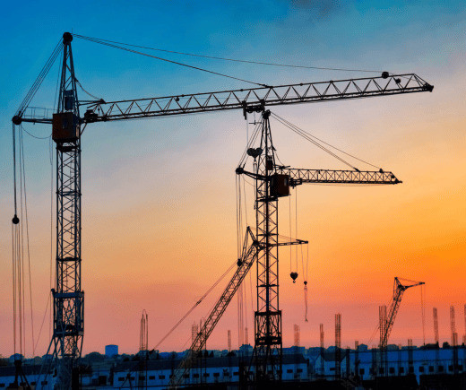 A striking sunset illuminates construction cranes, representing CUBE RegPlatform's extensive coverage in diverse industries